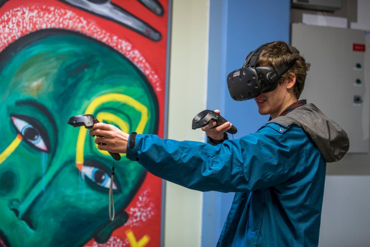 Ein mann står med VR-brillar og kontrollarar framfor eit kunstverk.