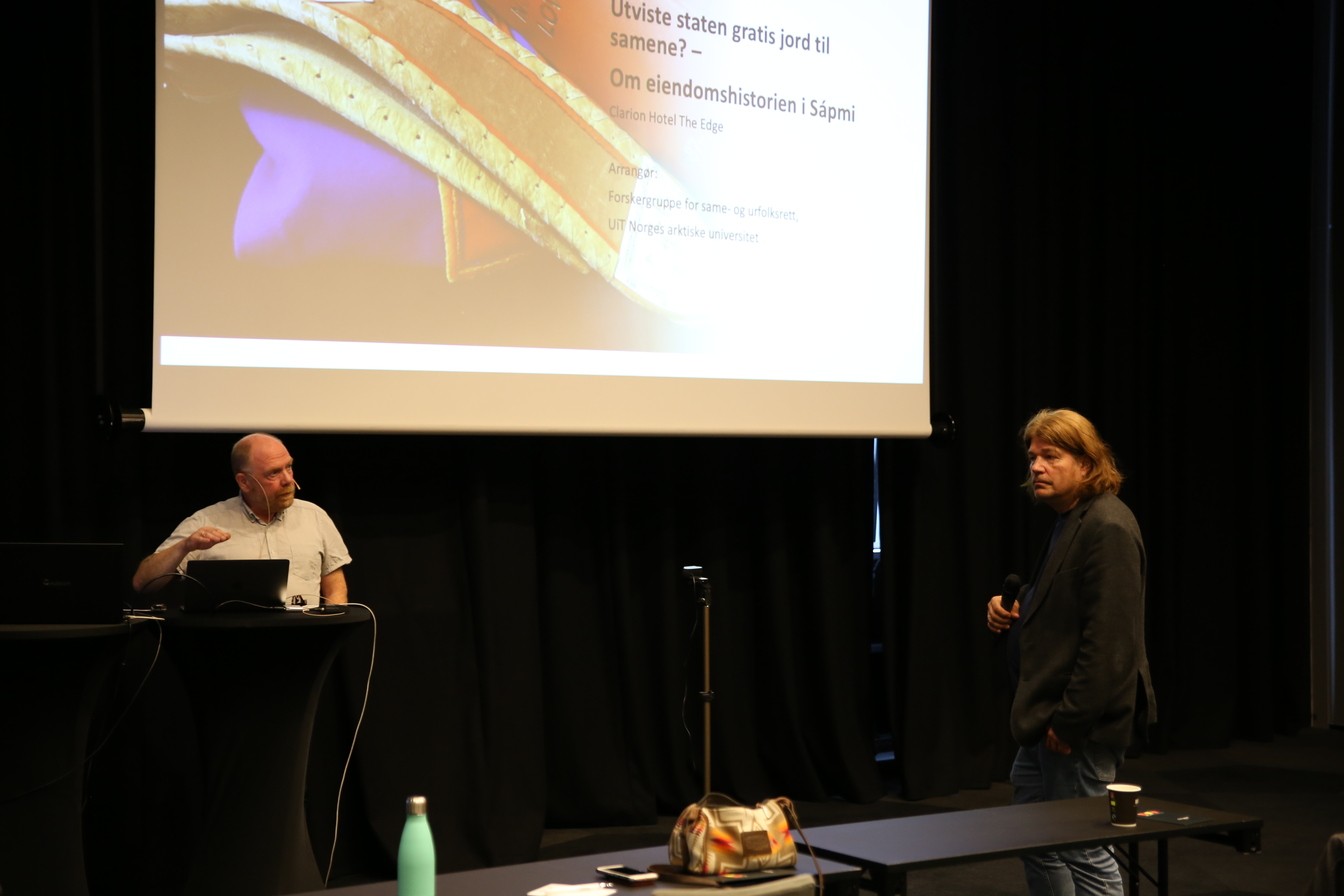 Gunnar Eriksen og Harald Lindback er i samtale. De st&aring;r begge foran et lerret med en presentasjon p&aring;. 