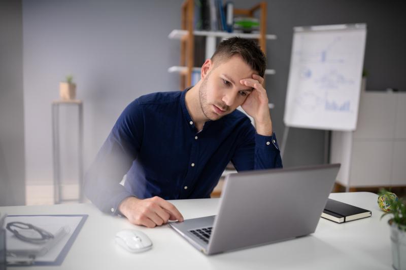 stressful-business-man-working-on-laptop.jpg MAnn sitter med hode i hånden og ser sliten ut foran laptop