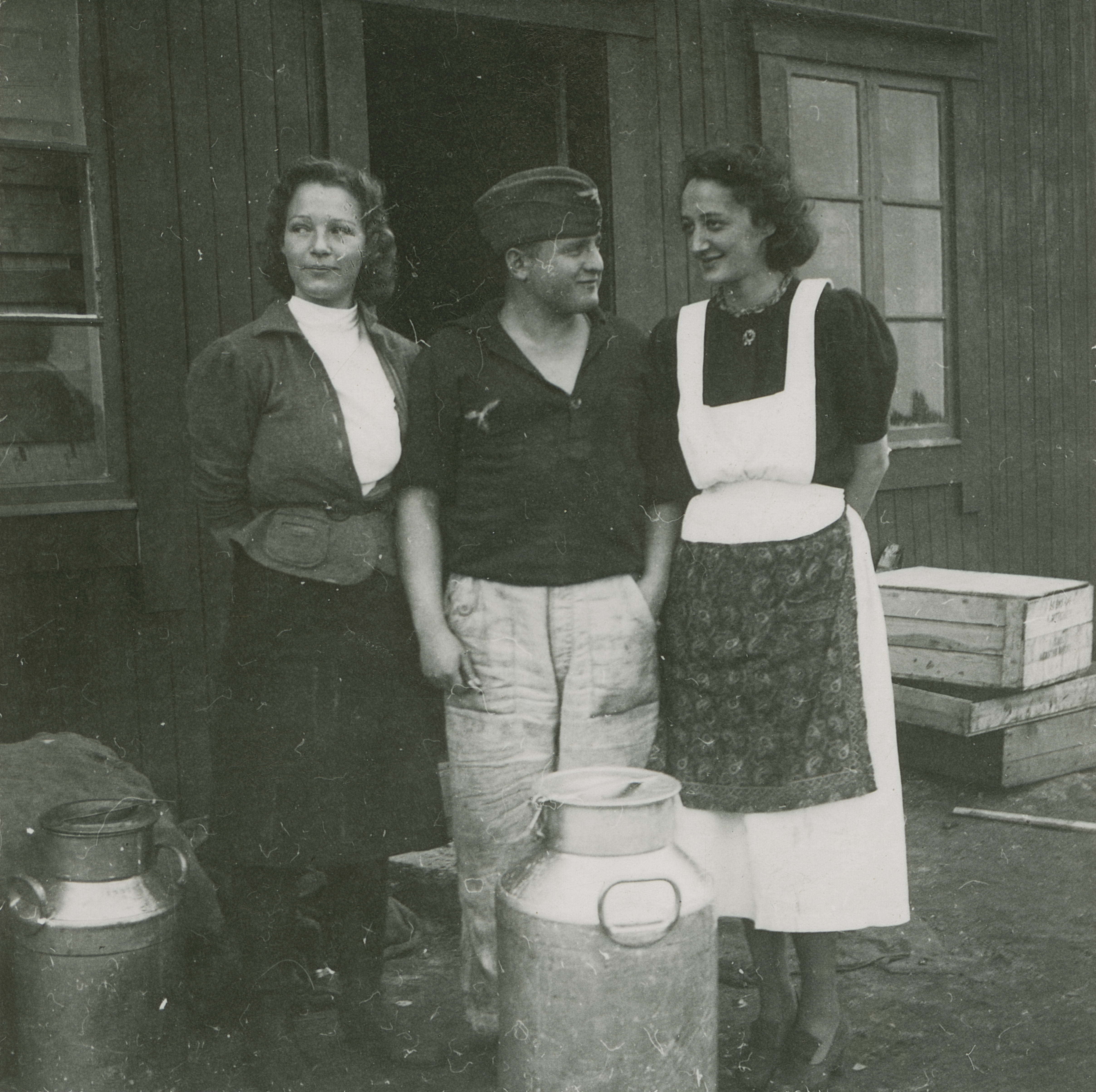 2.16.7 23912 Bodø flyplass 1940. Luftwaffe-soldat i arbeidsuniform foran brakke, flankert av to norske kvinner, trolig kjøkkenhjelper.jpg