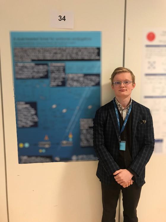 Stian is standing next to his poster. The poster has been blurred.