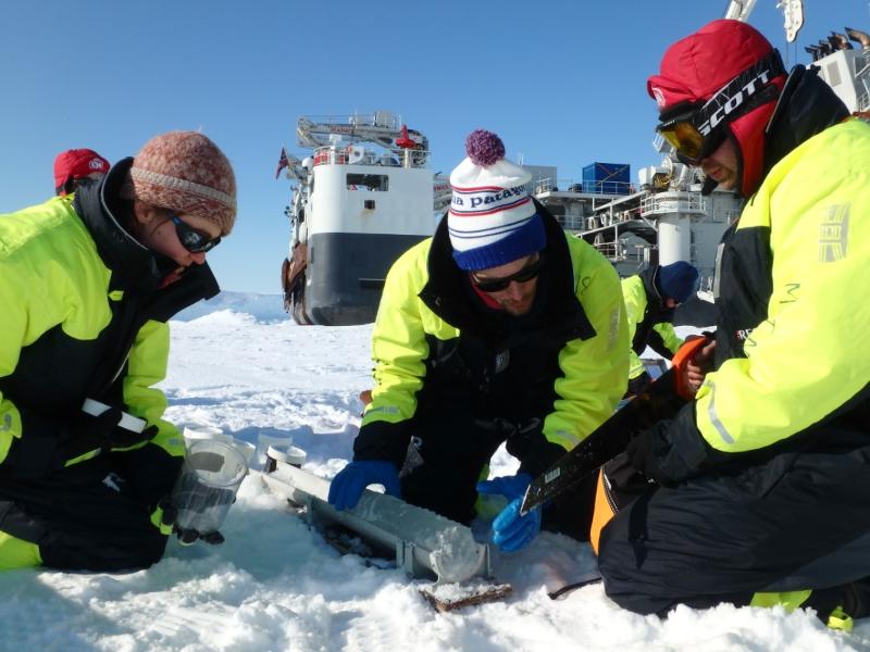 Tre godt kledde menneske held på med ein tingest på havis. Ei stor skute i bakgrunnen.