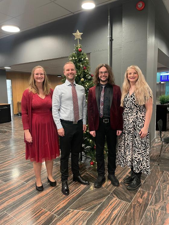 Members of the Haugland group, smiling and dressed up, standing in front of a Christmas tree.