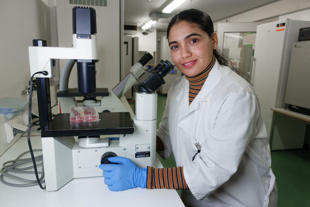 A woman in a lab coat posing with a microscope