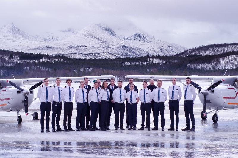 En rekke unge mennesker i flyveruniform poserer mellom to småfly på en rullebane om vinteren.