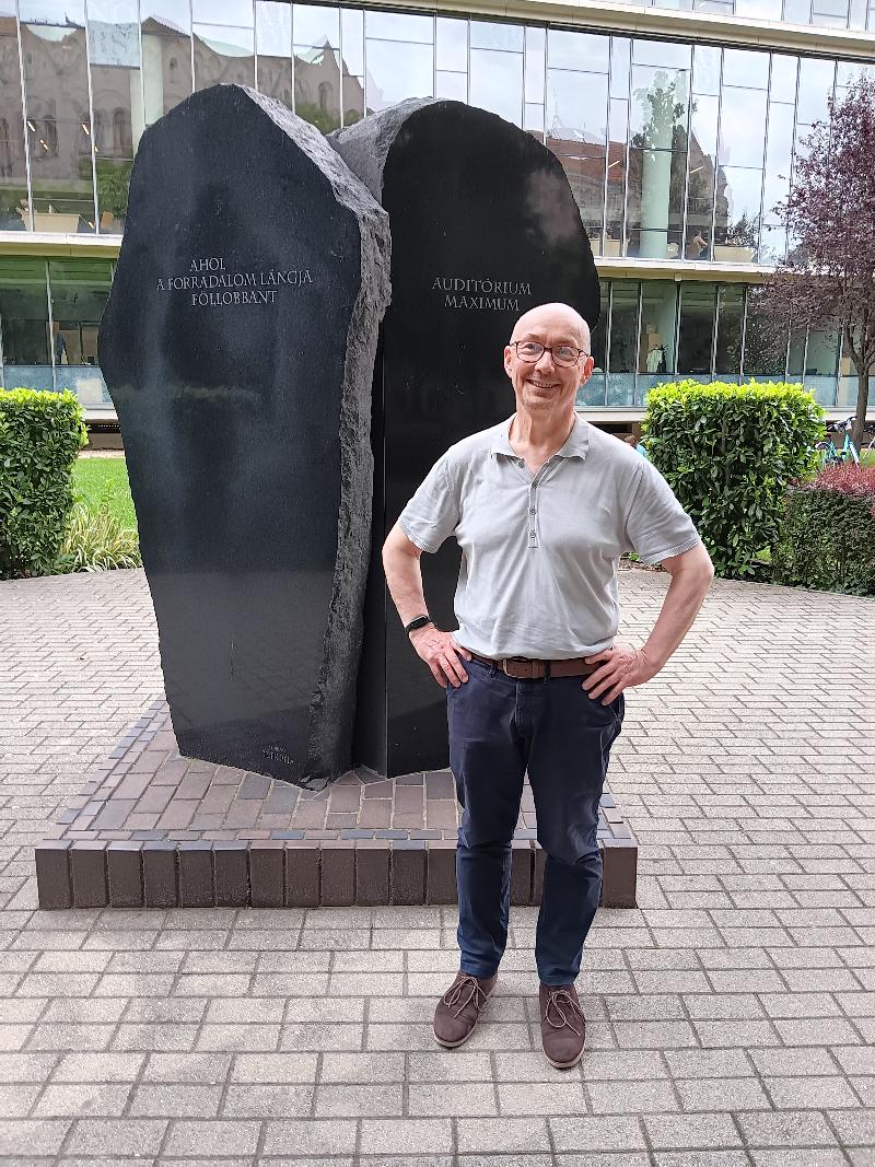 Man standing next to a stone monument, in a park.