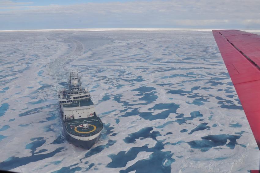 View feom insade a plane, looking down on a large ship in icy waters