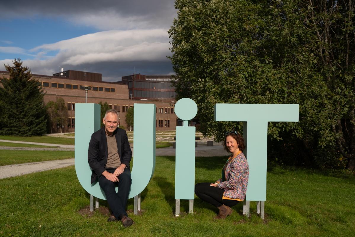 A man and a woman sitting inside a statue of the UiT letters.