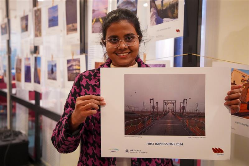 A smiling student holding up a picture of masts and gray clouds