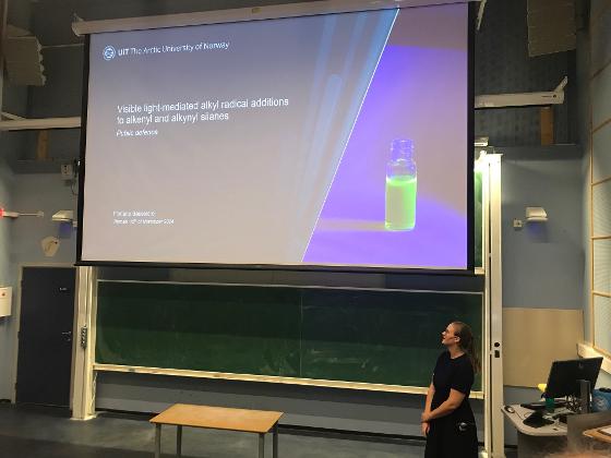 Floriane standing in front of a projector screen showing the title slide of her defence lecture