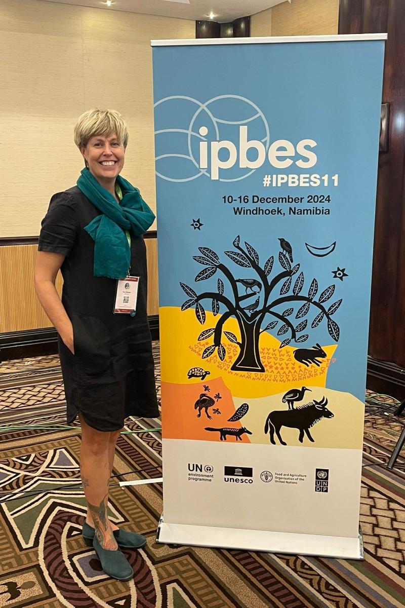 A smiling woman poses next to a poster for IPBES