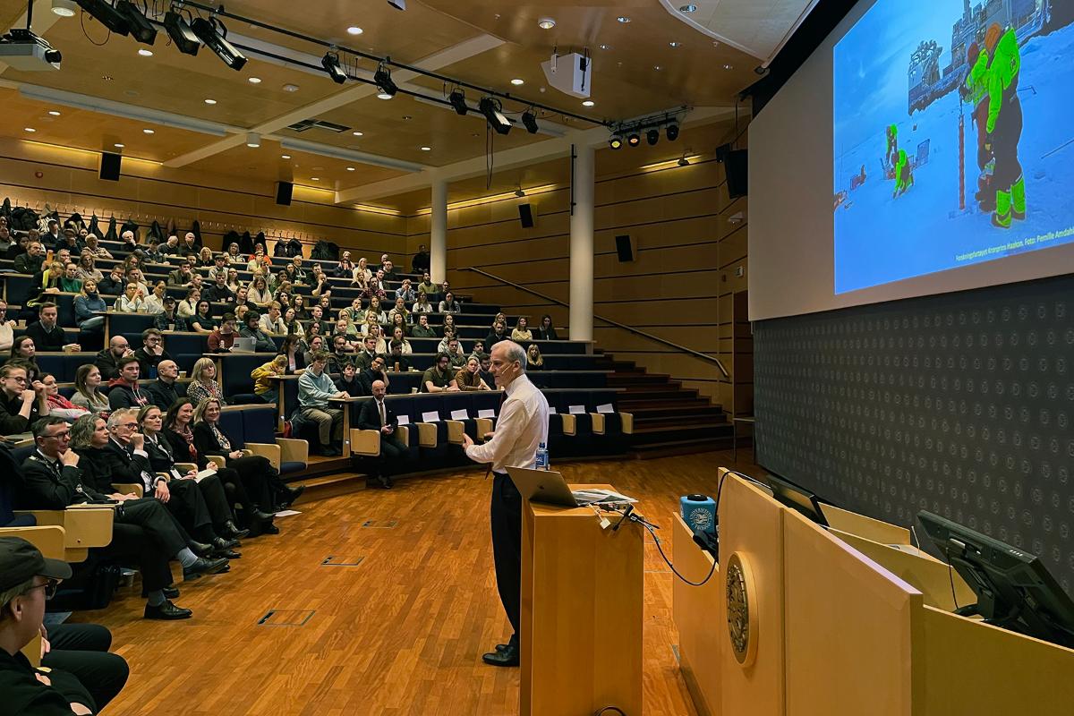 Mann står foran en fullsatt sal.