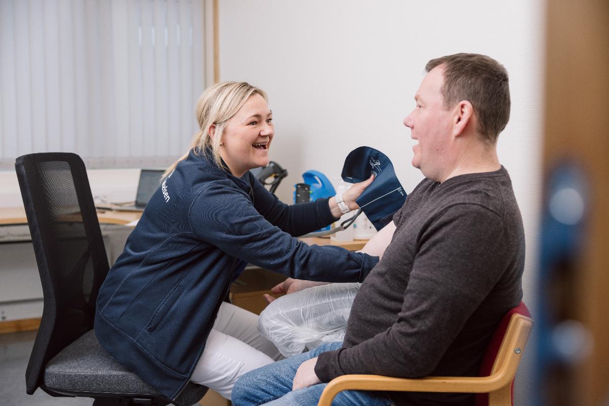 Pasient blir unders&oslash;kt av lege p&aring; legekontor. Begge ler.