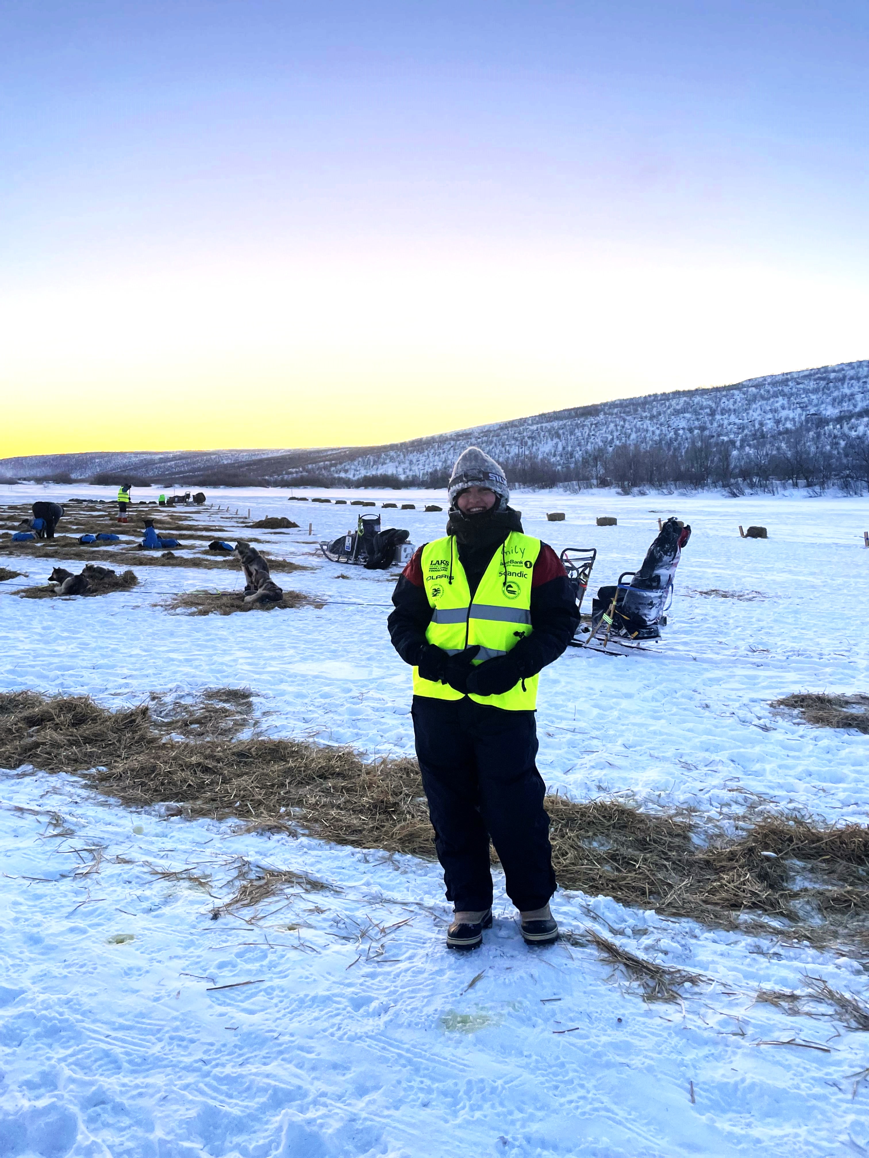 Dame st&aring;r ute med huskyer som hviler bak henne