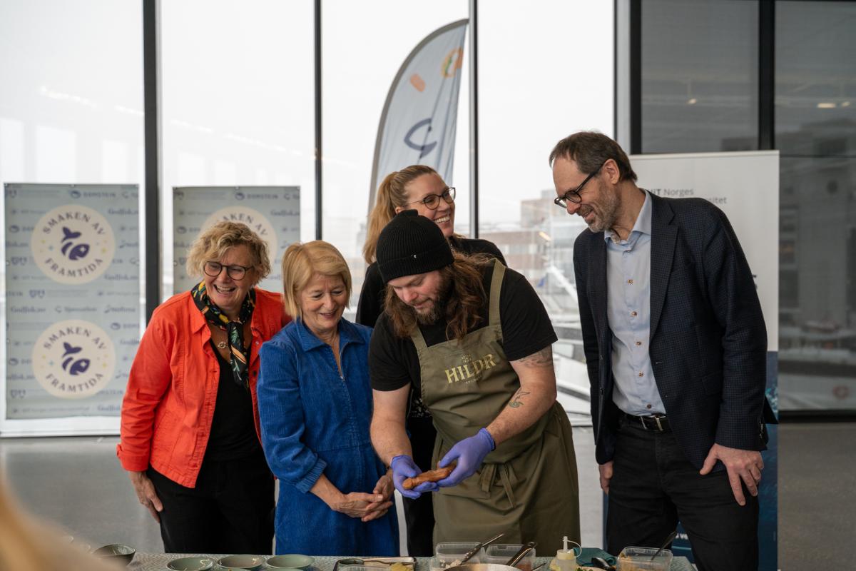 Flere personer samlet rundt bord der det blir servert sj&oslash;mat