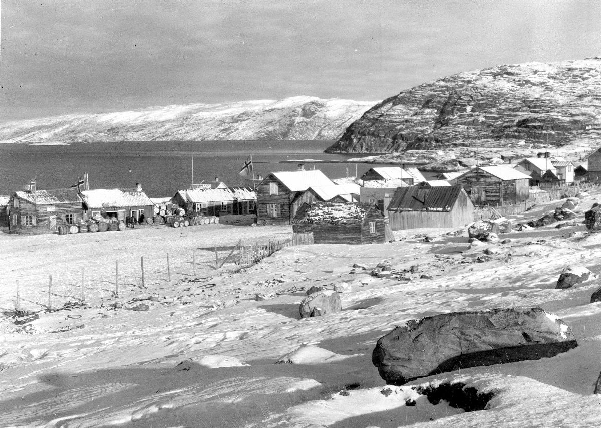 Vinterbilde av Bossekop fra 1928. Flere trehus der noen har heist det norske flagg. 
