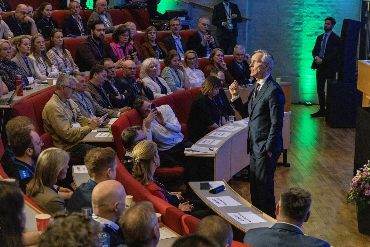 Mann snakker til forsamling i auditorium