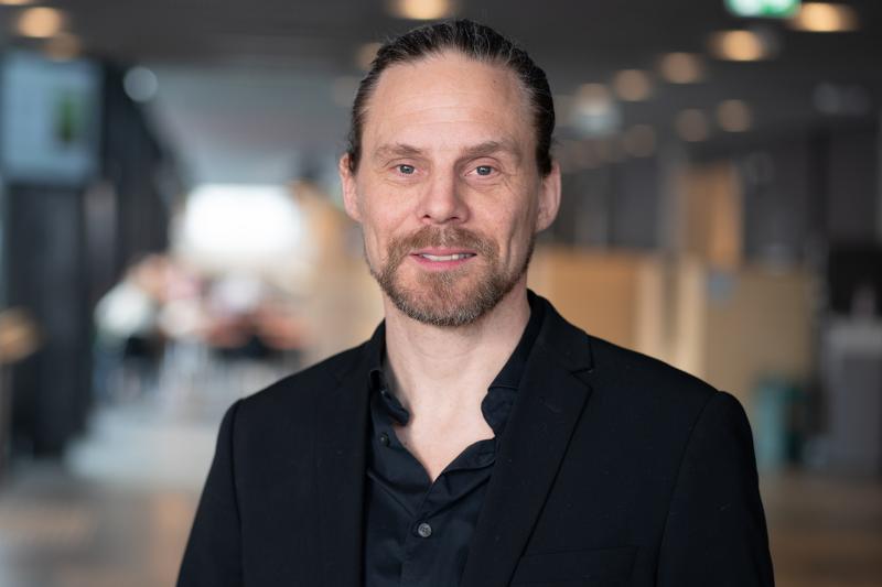 Jonas_Jakobsen_UIT_27802_Foto_Jorn_Berger_Nyvoll.jpg Mann kledd i sort blazer og skjorte smiler forsiktig til kamera.