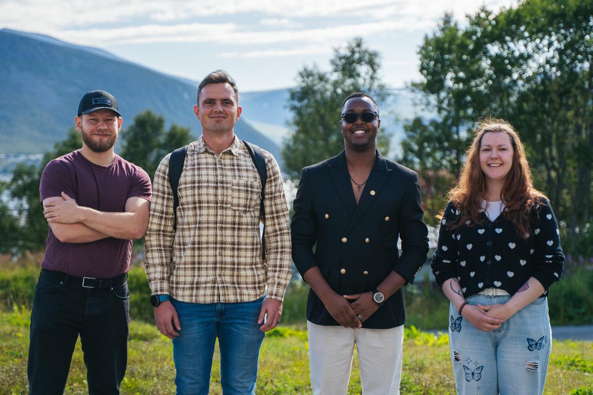 Fire studenter, tre gutter og ei jente smler mot kamera. De står ute og det er sommer