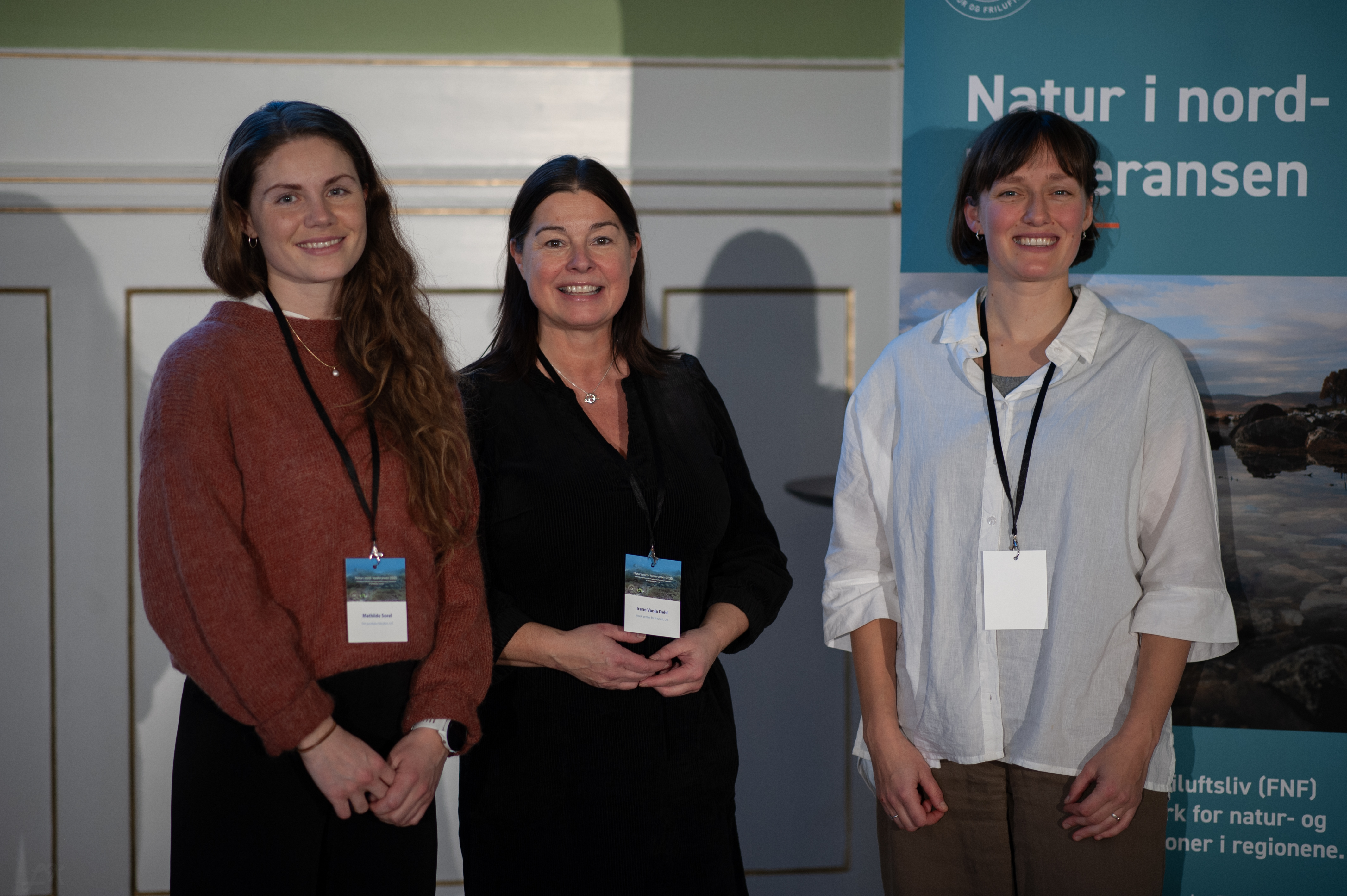 Tre kvinner står side om side og smiler til kamera. 