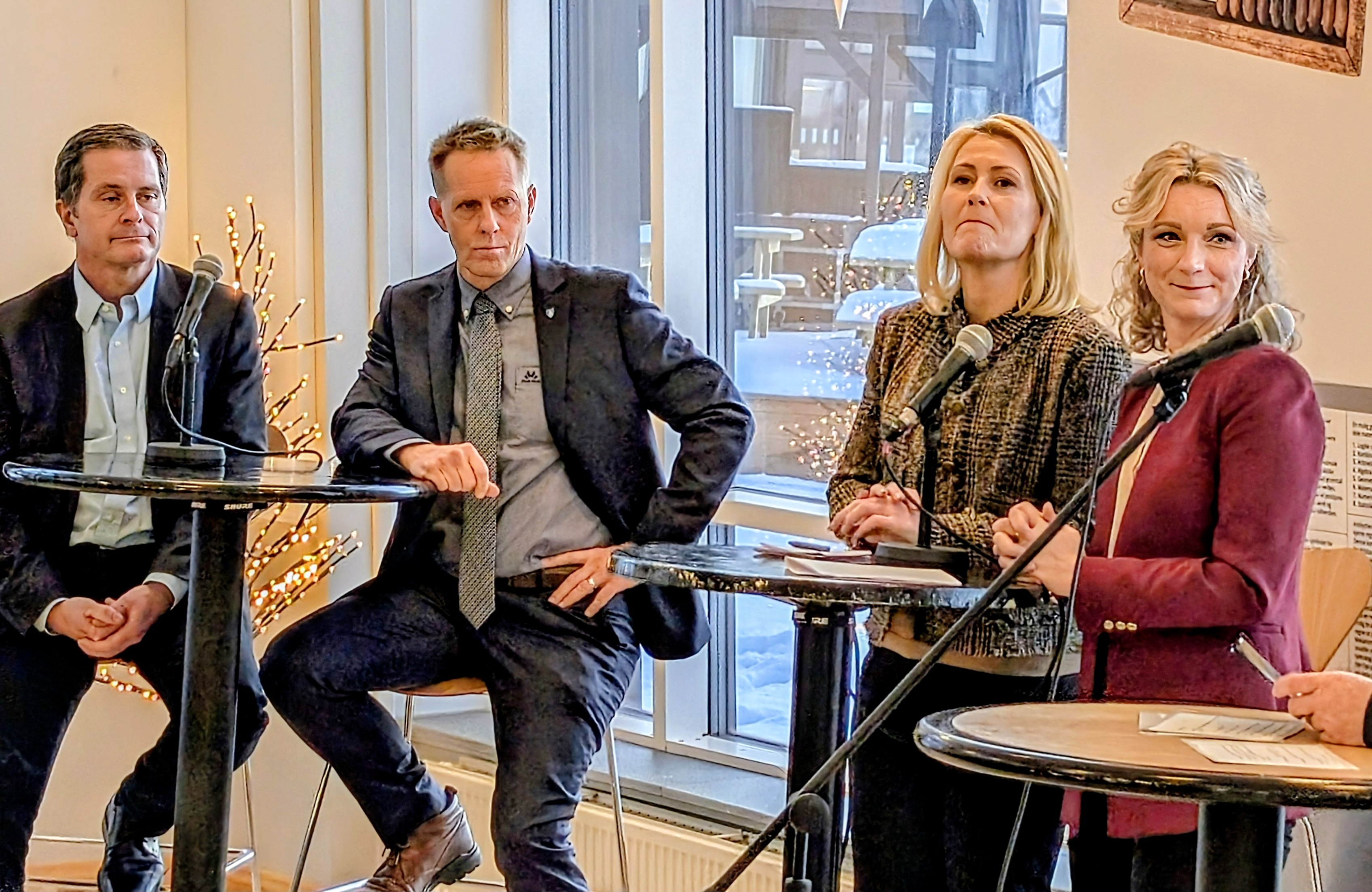 To personer som står, og to personer som sitter, rundt to bord.