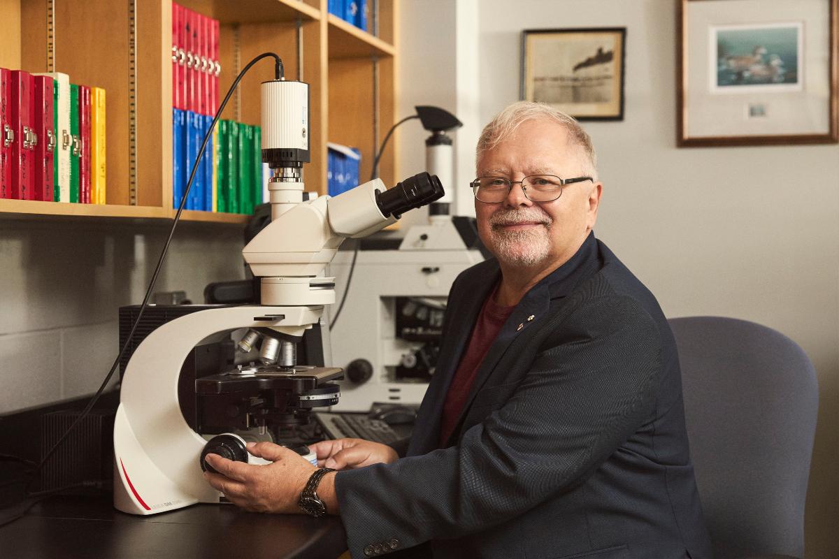 a smiling man with a microscope in a lab