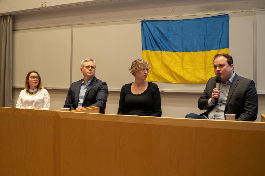 Four people sitting in a line along a table.