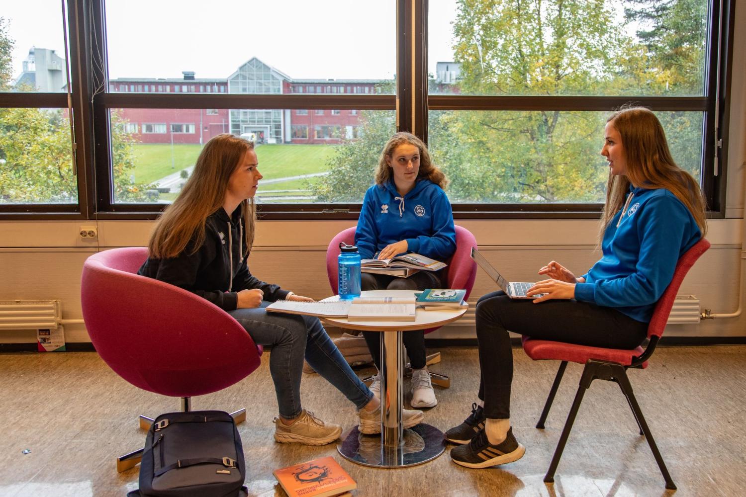 Tre jenter med volleyball treningsgensere p&aring; seg som sitter og jobber med studie.