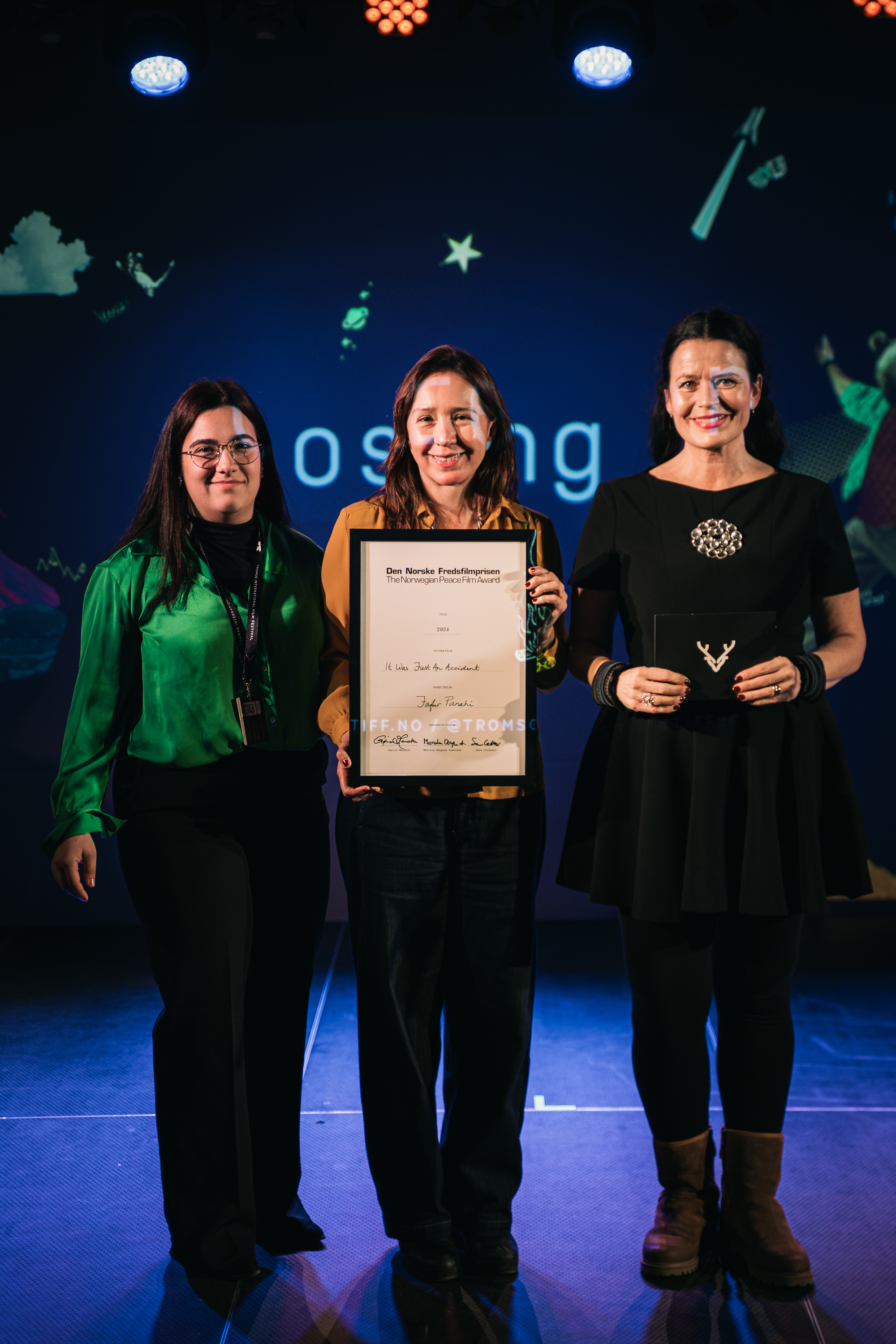 Three women on a stage holding a diploma.