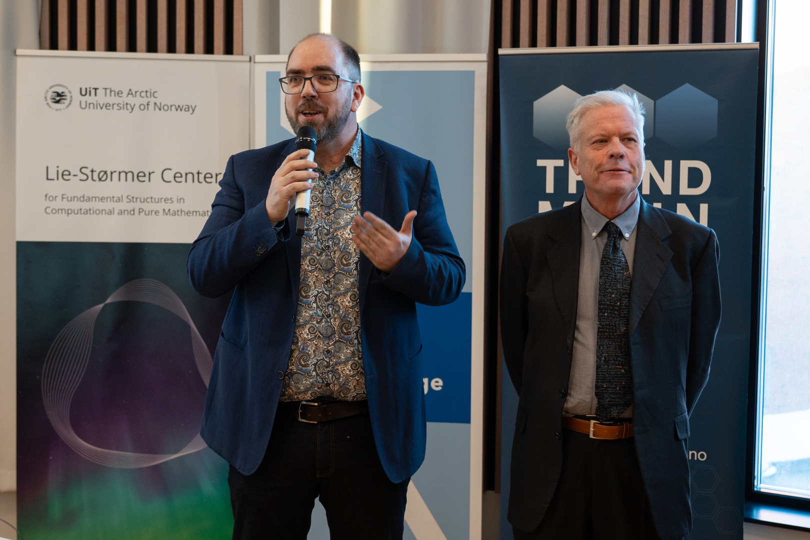 to menn som st&aring;r p&aring; en scene, den ene prater i mikrofon