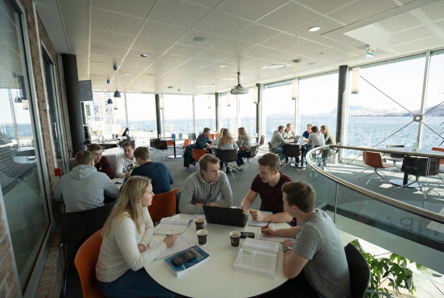 En gruppe studenter sitter samlet rundt et rundt bord i en lys og moderne kantine med store vindusflater.