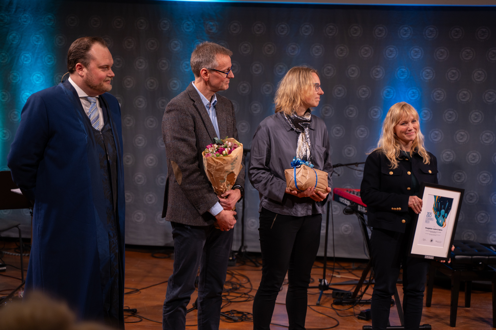 Utdanningsprisen-03715.jpg To damer og en mann mottar diplom, blomster og gave i staselig og feststemt universitetsauditorium. En rektor til venstre for dem.