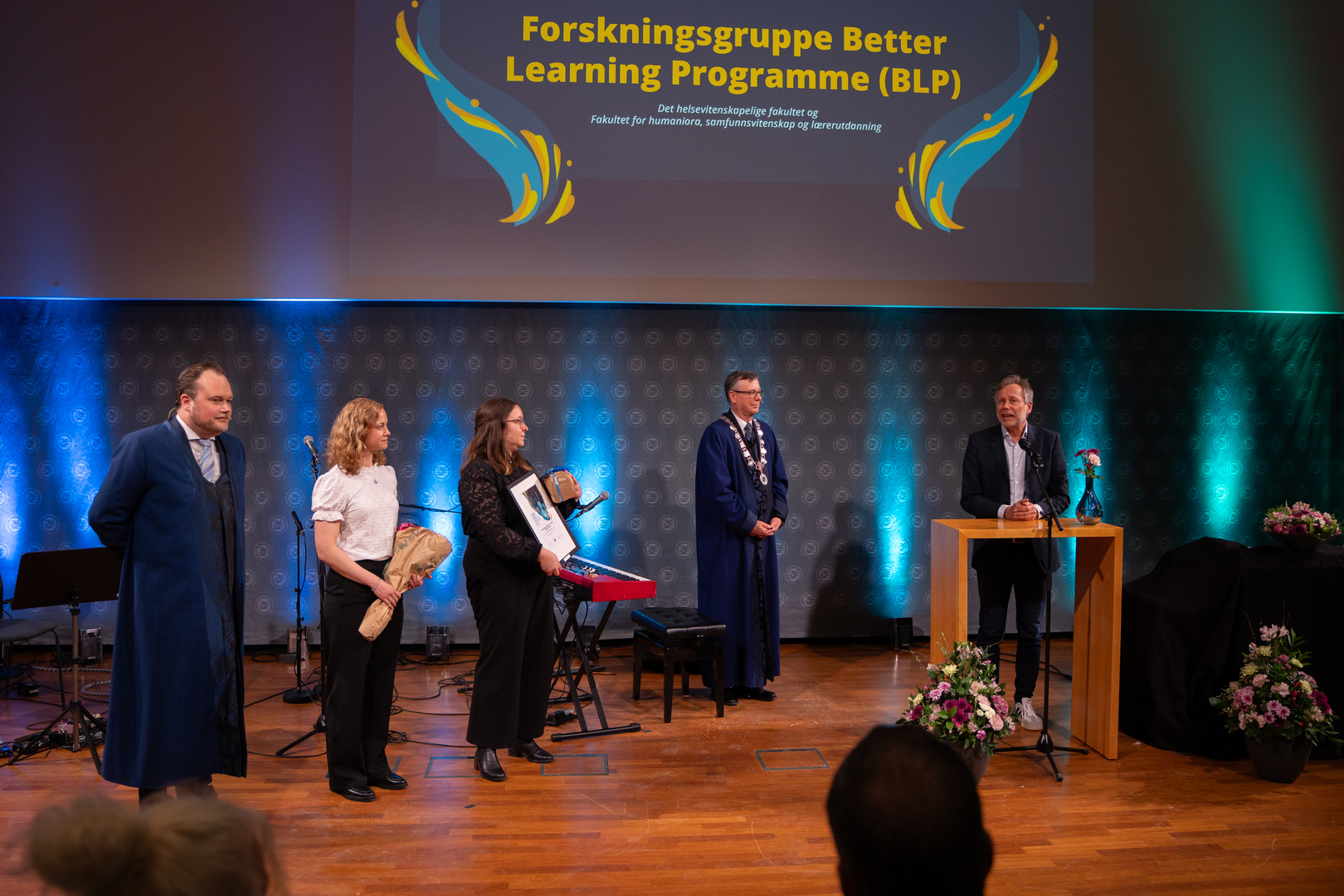 Innovasjonsprisen-03693.jpg En mann og to kvinner har mottatt diplom, blomster og gave i staselig og feststemt universitetsauditorium. To rektorer står på hver sin side av prisvinnerne.