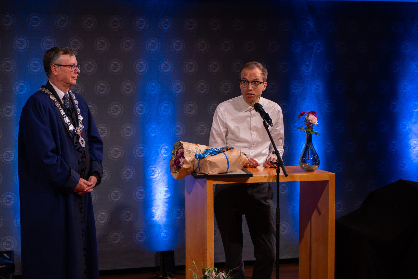 Ung forsker-03700.jpg Mann mottar diplom, blomster og gave i staselig og feststemt universitetsauditorium.