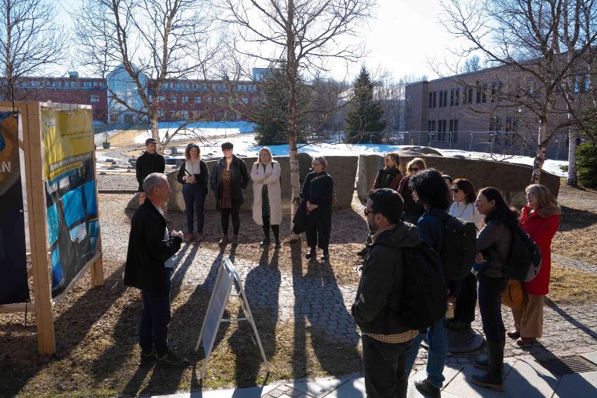 A group of people in a circle listening to a presentation of an outdoor exhibition.