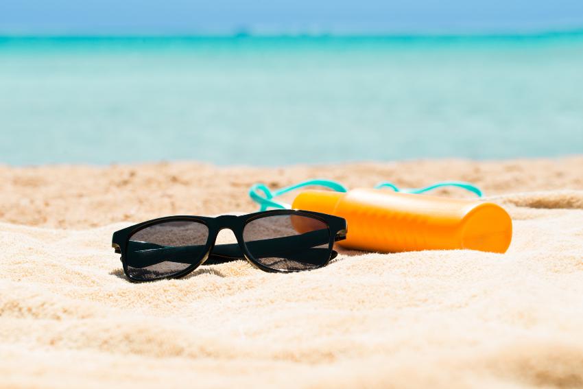 solbriller og solkrem som ligger p&aring; en strand 