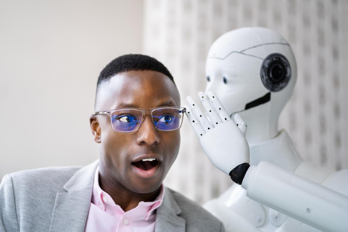 robot som visker noe i &oslash;ret til en mann med m&oslash;rk hudfarge og briller
