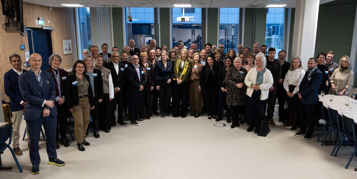 Gruppefoto med flere rader med personer samlet i et stort rom.